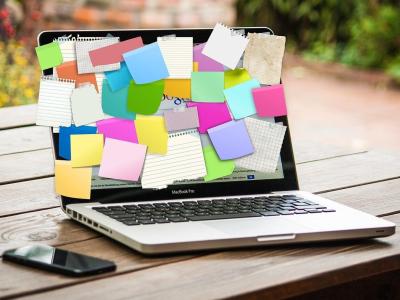 Laptop bedekt met kleurrijke notitieblaadjes op een tafel, met een smartphone ernaast.
