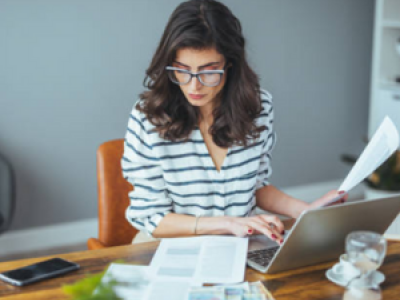 Vrouw werkt op laptop met documenten en calculator aan bureau in moderne kantooromgeving.