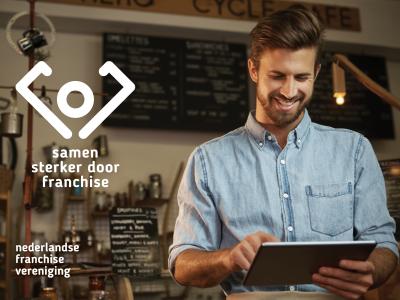 Man in een winkel gebruikt een tablet, met logo en tekst Nederlandse Franchise Vereniging op de achtergrond.