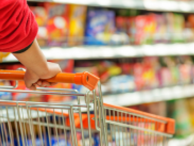 Iemand duwt een winkelwagen in een supermarktgang vol kleurrijke producten.