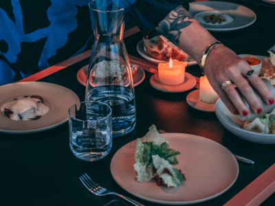 Hand plaatst een gerecht op een met liflafjes gedekte eettafel met kaarsen en een karaf water.