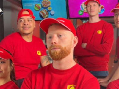 Medewerkers in rode bedrijfskleding poseren samen in een kleurrijke fastfoodomgeving.