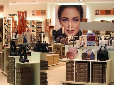 Interieur van een luxe tassenwinkel met uitgestalde handtassen, schoenen en reclameposters.