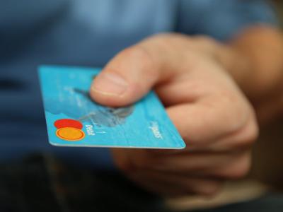 Een hand houdt een blauwe bankkaart vast, klaar om te worden overhandigd voor betaling.