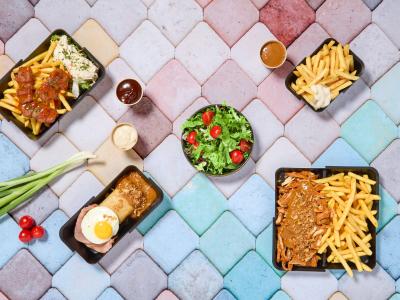 Diverse gerechten met friet, salade en sauzen gepresenteerd op een kleurrijke tegelachtergrond.