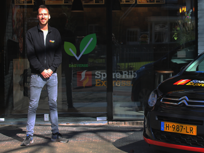 Bastiaan Brinkman staat voor een Spare Rib Express vestiging naast een geparkeerde bedrijfsauto.