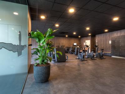 Moderne fitnessruimte met diverse cardio-apparaten, een grote plant en een glazen wand met silhouet.