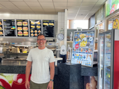 Een man staat glimlachend voor de toonbank in een moderne fastfood- of snackbaromgeving.