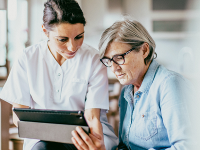 Zorgprofessional helpt oudere vrouw met een tablet in een huiselijke omgeving.