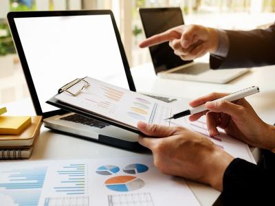 Twee personen bespreken financiële grafieken op papier en laptop op een bureau.