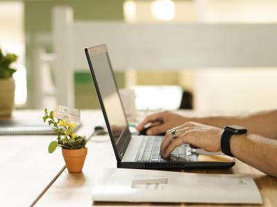 Persoon werkt op een laptop aan een houten bureau met planten en documenten als decoratie.