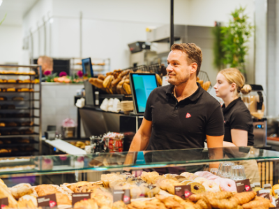 Twee medewerkers achter de toonbank met diverse gebakjes en broden in een Bakker Bart winkel.