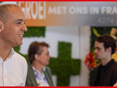 Twee zakenmannen in gesprek tijdens een franchisebeurs, met groene decoratie op de achtergrond.