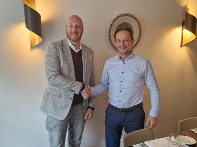 Twee mannen schudden elkaar de hand in een restaurant, omringd door sfeervolle verlichting en gedekte tafels.