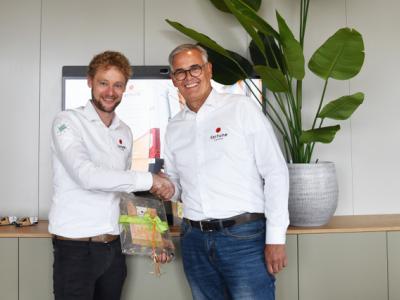 Twee mannen in Fortune Coffee-kleding schudden handen met een geschenk in een kantooromgeving.