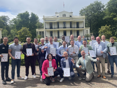 Groep mensen met certificaten viert de eerste verjaardag van Boomerang voor een historische villa.