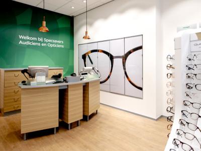 Interieur van een Specsavers-winkel met balie, groene welkomstmuur en display met verschillende brillen.