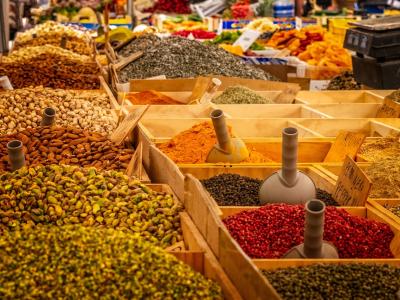 Kleurrijke specerijen en noten in houten bakken op een markt; benadrukt lokale variëteit en versheid.