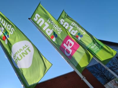 Groene PLUS-vlaggen voor een supermarkt die ook als ophaalpunt en drogisterij fungeert.