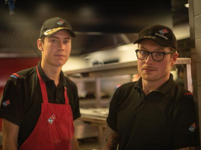 Twee Domino's-medewerkers in uniform staan in een keukenomgeving.