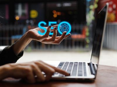 Hand boven laptop met zwevende tekst SEO en een tandwiel-icoon.