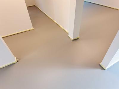 Een strak aangebrachte gietvloer in een ruimte met lichte wanden en kolommen.