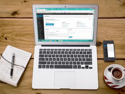 Laptop met een open WordPress-dashboard naast notitieboekje, pen, smartphone en espresso op houten tafel.