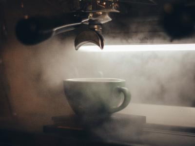 Espressomachine in werking met een kopje eronder dat omgeven is door damp.