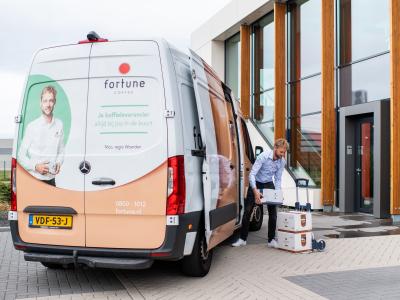 Fortune Coffee-leverancier laadt dozen uit een bestelwagen bij een modern kantoorgebouw.
