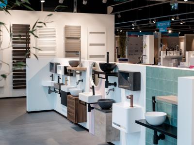 Een moderne showroom met verschillende wastafels en radiatoren gepresenteerd tegen een witte en groene tegelwand.