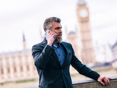 Man in een pak voert een telefoongesprek voor iconische Londense gebouwen, waaronder de Big Ben.