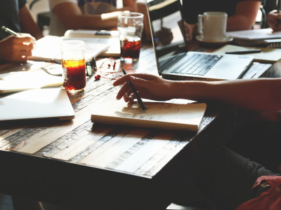 Mensen werken samen aan een tafel met laptops, notitieboeken en drankjes, wat samenwerking in planning suggereert.