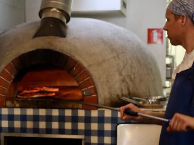Pizzachef bakt pizza in authentieke houtoven bij De Pizzabakkers Hilversum.