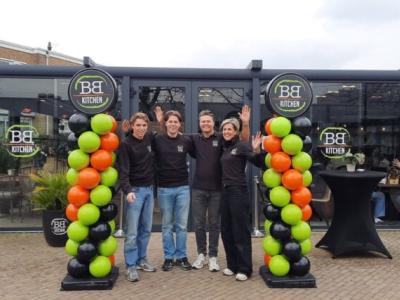 Vier medewerkers poseren lachend bij de entree van de 40e Big Bread Kitchen vestiging, omringd door ballonpilaren.