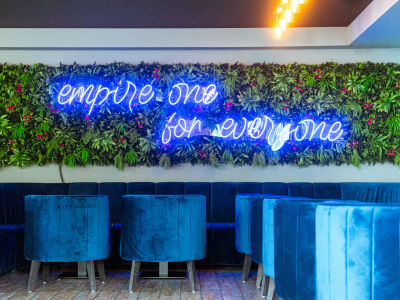 Kunsthaag met neontekst empire one for everyone boven luxe blauwe zitplekken in een chique interieur.