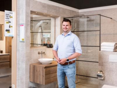 Man in een moderne showroom van Sanidirect Middelburg, met badkamermeubels en accessoires op de achtergrond.