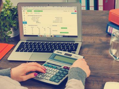 Persoon gebruikt rekenmachine en laptop met financiële gegevens op bureau voor debiteurenbeheer.