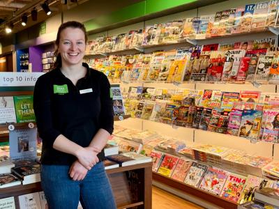 Medewerkster van ReadShop Lisse staat glimlachend voor een rek met tijdschriften en boeken in de winkel.