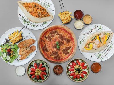Assortiment van pizza, salades, gerechten met friet en diverse sauzen, gepresenteerd op een grijze tafel.