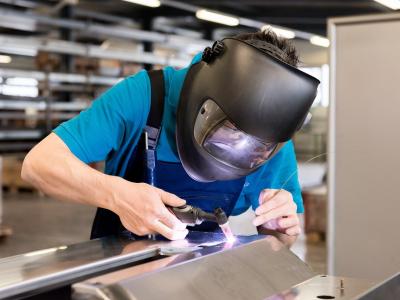 Een lasser met beschermend gezichtsmasker is bezig met het lassen van een metalen object in een werkplaats.