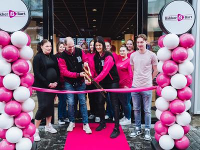 Feestelijke heropening van Bakker Bart Enschede met lintknippen, omringd door medewerkers en roze-witte ballondecoraties.