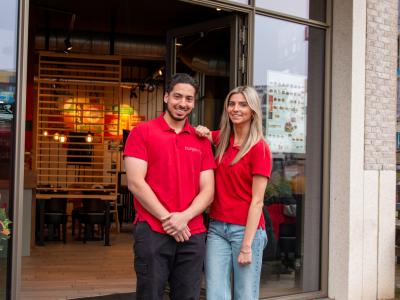 Twee medewerkers in rode shirts staan voor de ingang van een Burgerme restaurant.