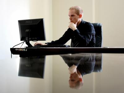 Man in een zakelijke outfit werkt geconcentreerd achter een computer aan een bureau in een kantooromgeving.