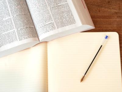 Open wetboek naast een leeg notitieboek met een pen op een houten bureau.