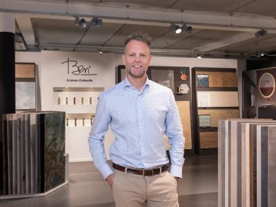 Man in een showroom van sanitairproducten, omringd door wand- en vloertegelmonsters.