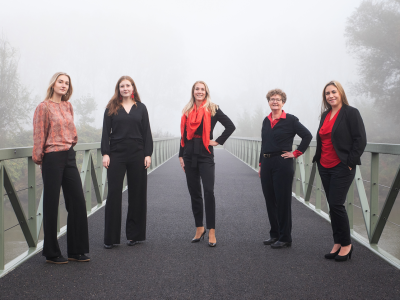 Vijf vrouwen in zakelijke kleding staan op een mistige brug, symbool voor samenwerking binnen franchise.