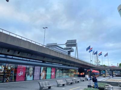 DA-winkel met opvallende gevelreclame op Schiphol, met vlaggen en passanten in de omgeving.