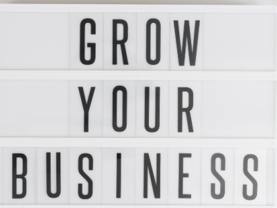 Lichtbak met de tekst Grow Your Business op een bureau met een notitieboek, smartphone en koffiekopje.
