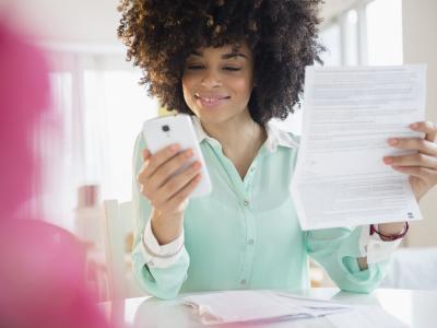 Persoon in kantooromgeving controleert documenten en gebruikt smartphone voor boekhoudkundige taken.