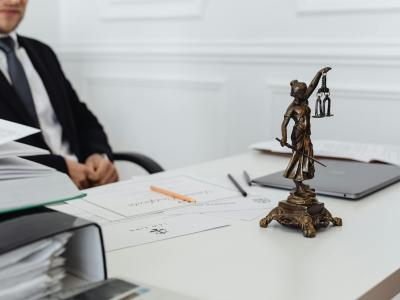 Een zakenman zit achter een bureau met daarop een Vrouwe Justitia beeld en diverse documenten.